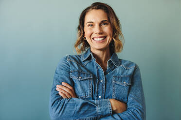 Portrait of a female entrepreneur in her 30s wearing business casual. This confident and successful business woman smiles at the camera as she stands in a studio with her arms crossed. - JLPPF02140