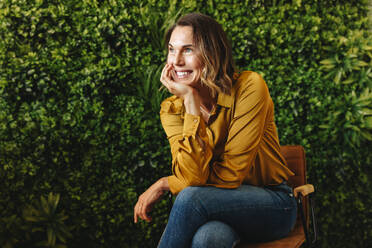 Female company owner smiles as she reflects on the eco-friendly goals she has for her organisation. Happy business woman working in a green office with a focus on success and sustainability. - JLPPF02164