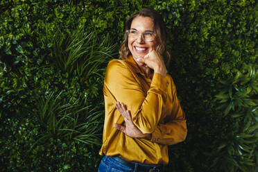 Businesswoman wearing a professional attire and eyeglasses stands representing the face of success and sustainability in her company. Happy female professional leading in an eco-friendly office. - JLPPF02166