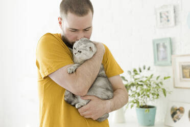 Man embracing and kissing cat at home - ONAF00576