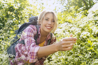 Lächelnde Frau pflückt Blumen im Wald - NDEF00879