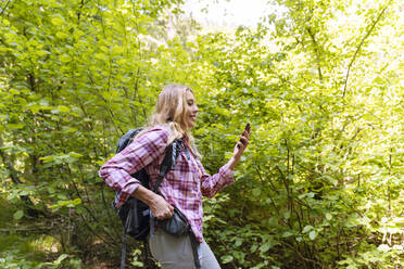 Lächelnder Wanderer mit Smartphone im Wald - NDEF00886