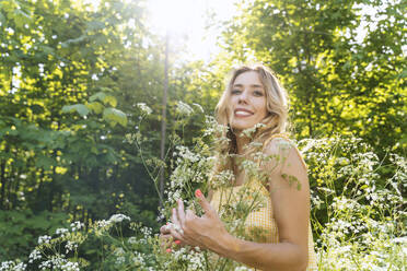 Lächelnde Frau steht inmitten von Blumen im Wald - NDEF00917