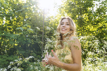 Smiling woman standing amidst flowers in forest - NDEF00917