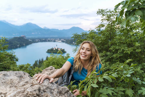 Lächelnde Frau beim Wandern über Felsen inmitten von Pflanzen - NDEF00954