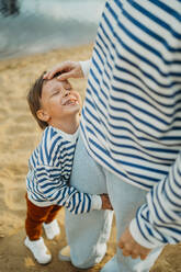 Mutter streichelt glücklichen Sohn am Strand - ANAF01691