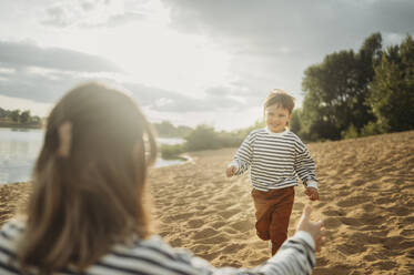 Lächelnder Sohn läuft am Strand auf seine Mutter zu - ANAF01694