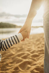 Mutter und Sohn halten sich am Strand an den Händen - ANAF01696