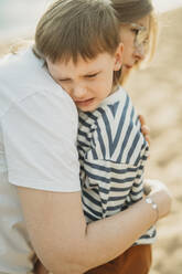 Mother embracing sad son at beach - ANAF01699