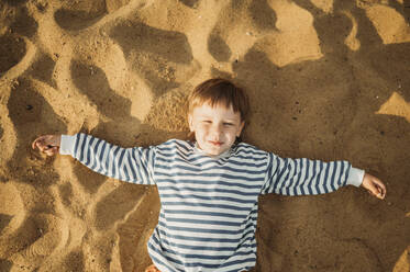 Smiling boy lying on beach sand - ANAF01700