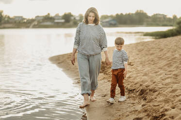 Mother and son walking near shore at beach - ANAF01708