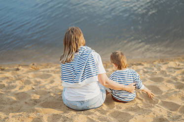 Blonde Mutter und Sohn sitzen am Strand - ANAF01710