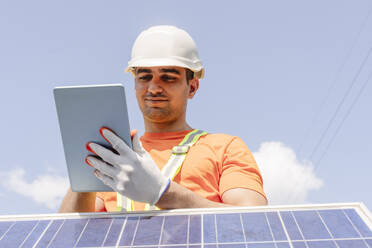 Ingenieur, der einen Tablet-PC neben einem Sonnenkollektor benutzt, mit dem Himmel im Hintergrund - OSF01832