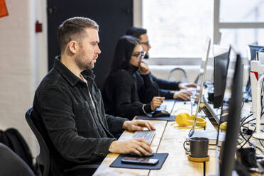 Geschäftsmann arbeitet am Computer mit Kollegen im Hintergrund - WPEF07435