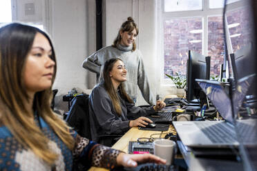 Lächelnde Geschäftsfrau mit Kollegen, die an einem Computer am Schreibtisch arbeiten - WPEF07476