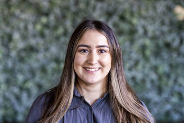 Happy young businesswoman with long hair in front of wall - WPEF07483