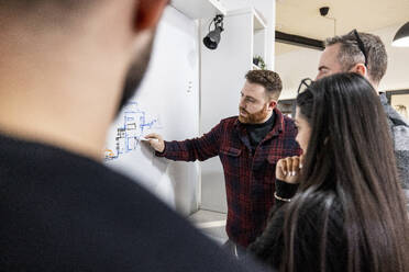 Businessman drawing on white board and explaining to colleagues in office - WPEF07516