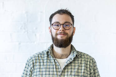 Smiling young businessman wearing eyeglasses in front of white wall - WPEF07520