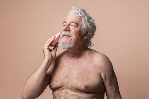Älterer Mann mit geschlossenen Augen bei der Hautpflege vor beigem Hintergrund - OIPF03142