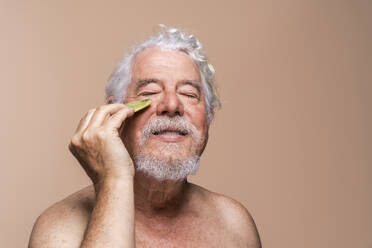 Älterer Mann mit geschlossenen Augen massiert Gesicht mit Gua Sha - OIPF03144