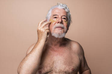 Hemdloser älterer Mann, der eine Augenklappe vor einem beigen Hintergrund anbringt - OIPF03150
