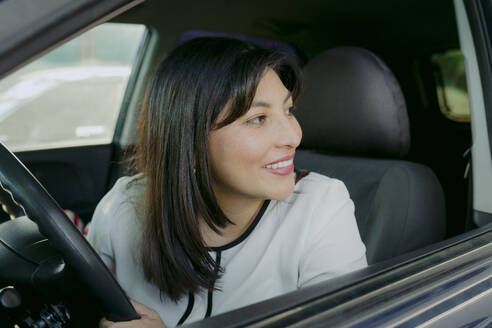 Lächelnde Frau mit schwarzen Haaren sitzt im Auto - DSIF00672
