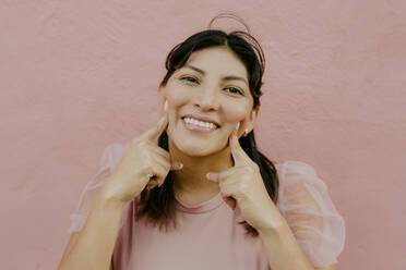 Glückliche Frau, die ihr Gesicht vor einer rosa Wand berührt - DSIF00677