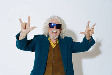 Happy senior man showing horn gesture against white background - OIPF03159