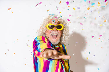 Fröhlicher älterer Mann mit Sonnenbrille, der sich an Konfetti vor weißem Hintergrund erfreut - OIPF03190