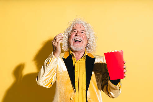 Cheerful senior man with box of popcorn against yellow background - OIPF03199