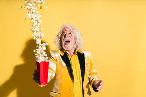 Fröhlicher älterer Mann, der Popcorns vor gelbem Hintergrund wirft - OIPF03201