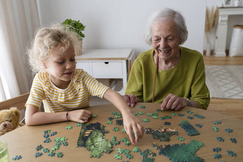 Smiling grandmother and granddaughter solving jigsaw puzzle - SVKF01481