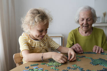 Enkelin und Großmutter beim Lösen eines Puzzles auf dem Tisch - SVKF01483