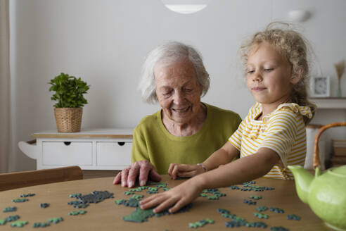 Großmutter und Enkelin lösen ein Puzzle auf einem Tisch - SVKF01486