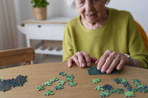 Ältere Frau löst ein Puzzle auf dem Tisch zu Hause - SVKF01487