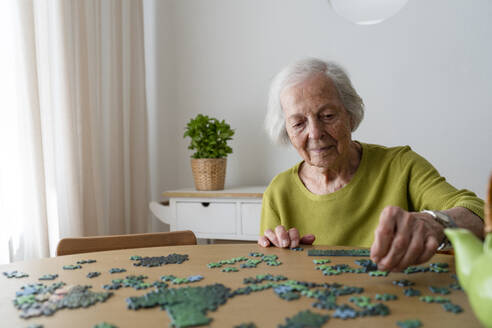 Ältere Frau löst ein Puzzle auf einem Tisch - SVKF01488