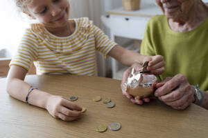 Smiling granddaughter putting coin in piggy bank - SVKF01492