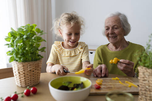 Lächelnde Großmutter und Enkelin begutachten Gemüse auf dem Tisch - SVKF01500
