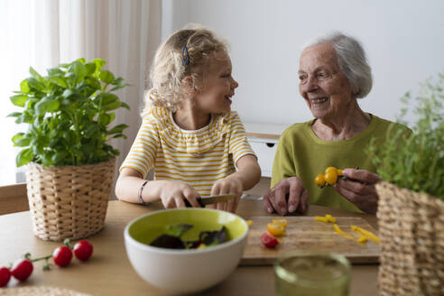 Lächelnde Großmutter und Enkelin halten Gemüse auf dem Tisch - SVKF01501