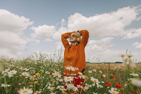 Woman with head in hands standing amidts flowers in chamomile field - VSNF01109