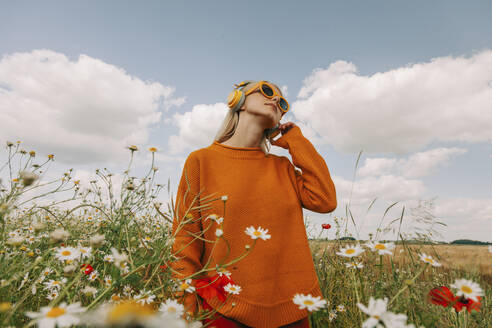 Woman listening to music standing in chamomile field - VSNF01110