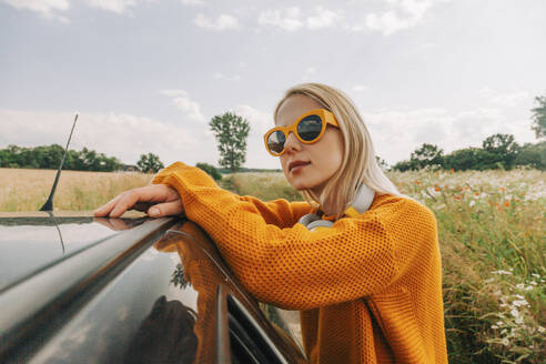 Woman wearing sunglasses leaning on car - VSNF01111