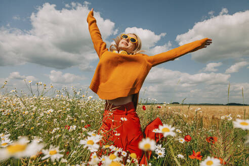 Carefree woman jumping with arms raised in chamomile field - VSNF01113