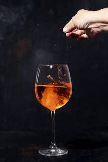 Hand einer Frau, die Eiswürfel in ein Glas Aperol Spritz gibt - SBDF04629