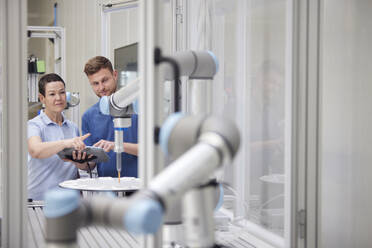 Technician explaining robotic machine to colleague in factory - RBF09039