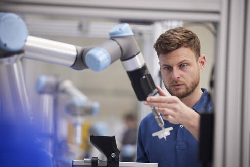 Focused engineer holding robotic arm in modern factory - RBF09053