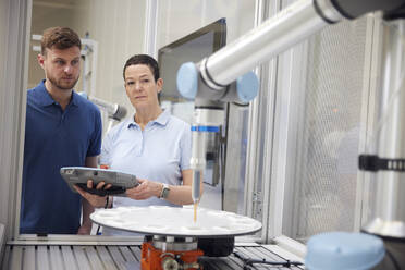 Colleagues examining robotic arm using equipment in industry - RBF09055