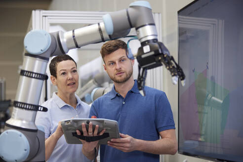 Colleagues discussing over robotic arm in modern factory - RBF09061