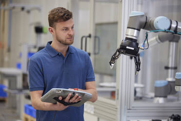 Techniker, der einen Roboterarm bedient, der Geräte in der Industrie verwendet - RBF09064