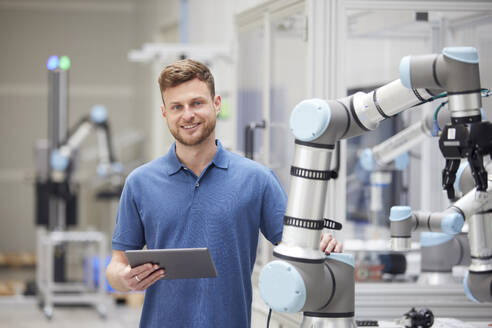 Smiling technician standing next to modern machine in industry - RBF09070